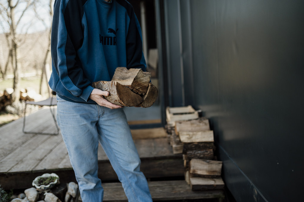 Person carries firewood near a cabin during day in a country setting