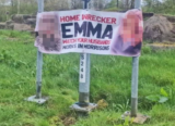 Banner calling out “home wrecker” with her face and work place on display is plastered by a roadside